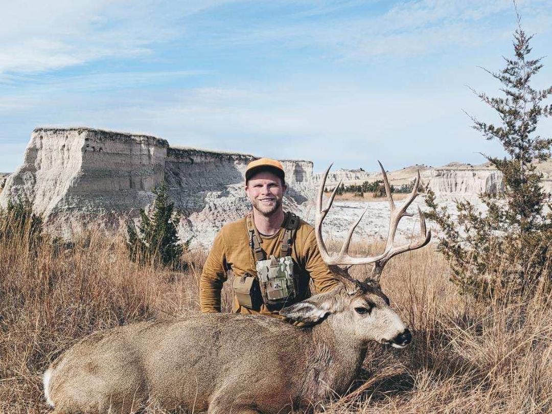 Hunter with a mule deer buck below South Dakota buttes
