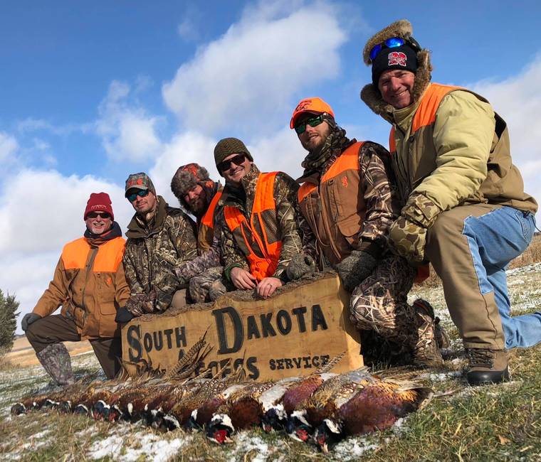 Group of hunters kneeling behind a long row of harvested pheasants