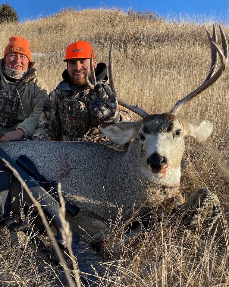 Two hunters in blaze orange with a mature mule deer buck