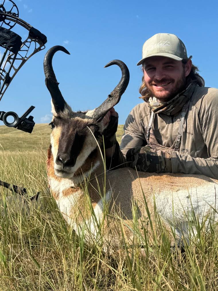 Hunter holding a pronghorn antelope by the horns in open country