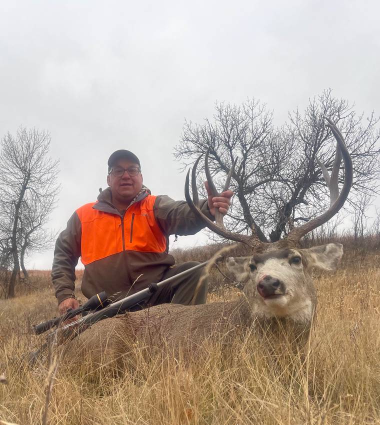 Hunter in blaze orange with a wide mule deer rack in prairie grass