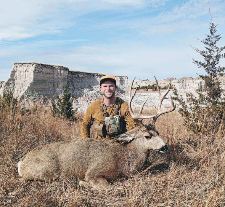 Hunter with a mule deer buck below South Dakota buttes