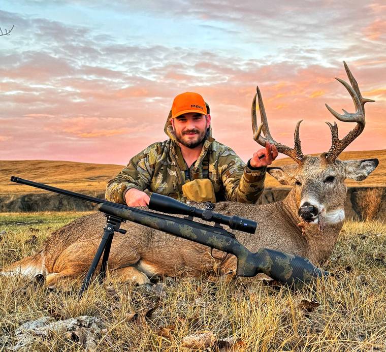 Rifle hunter with a mule deer buck at sunset on the prairie
